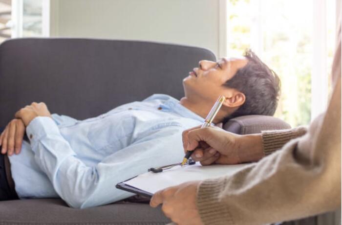 A client reclining on a sofa while a facilitator takes gentle notes